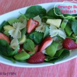 spinach salad with pasta, pineapple, strawberries in a white bowl