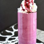 A purple milkshake in a glass with whipped cream and a cow straw.