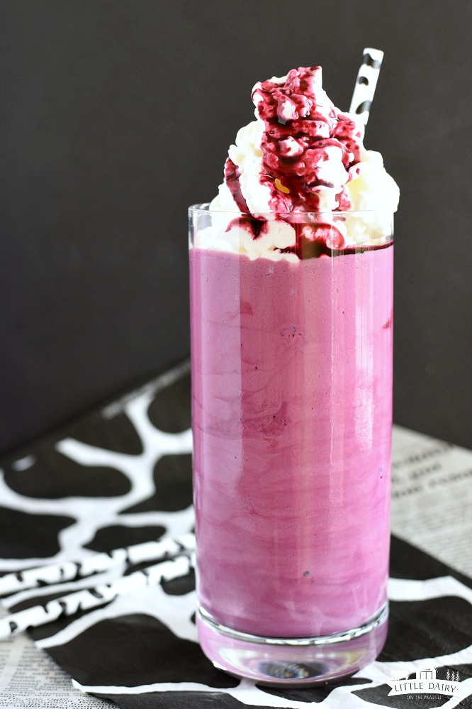 A purple milkshake in a glass with whipped cream and a cow straw.