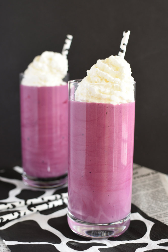 two purple milkshakes in glasses with whipped cream on top, on a cow spotted napkin
