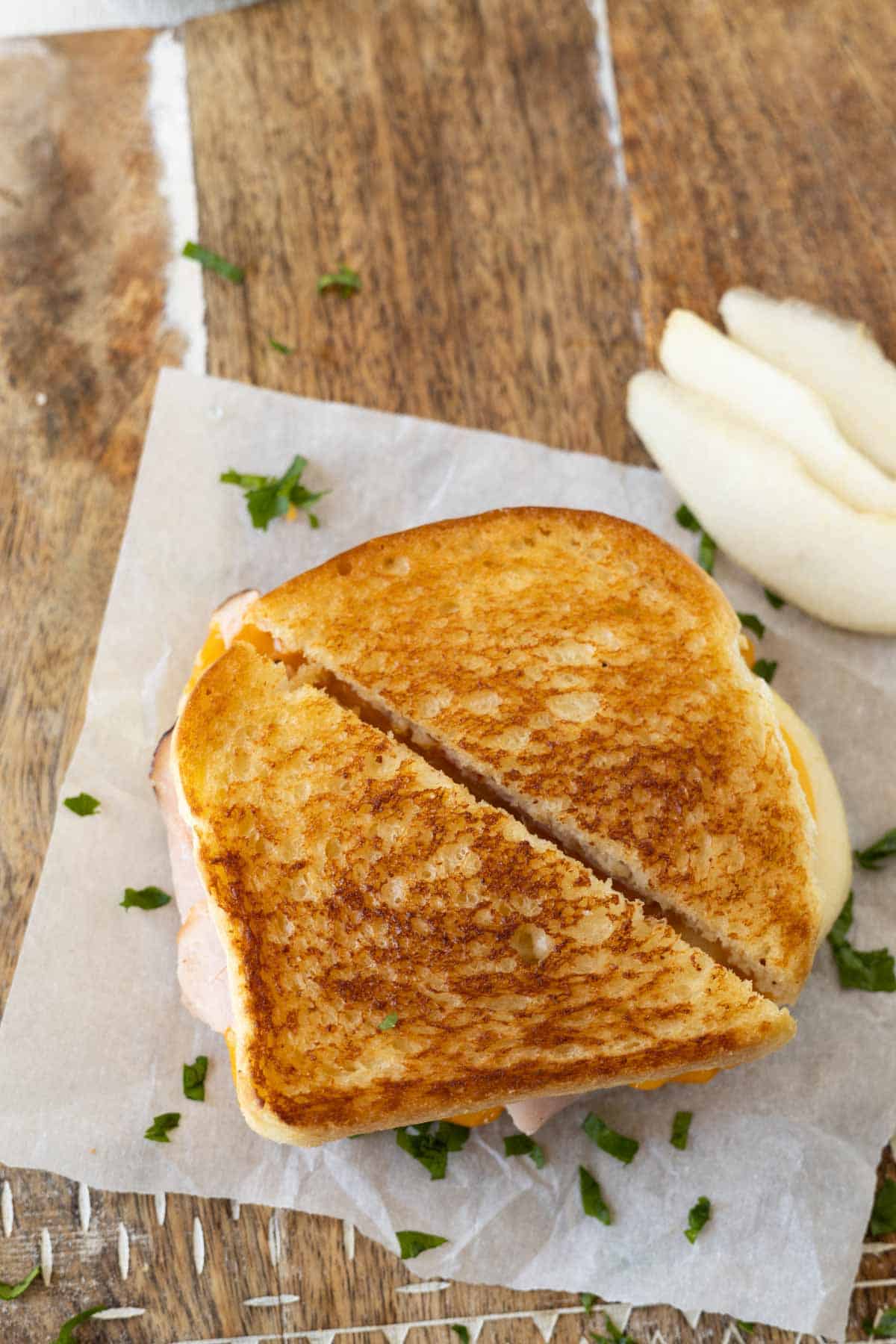 A toasted grilled cheese sandwich cut in half with sliced pears on a wooden cutting board.