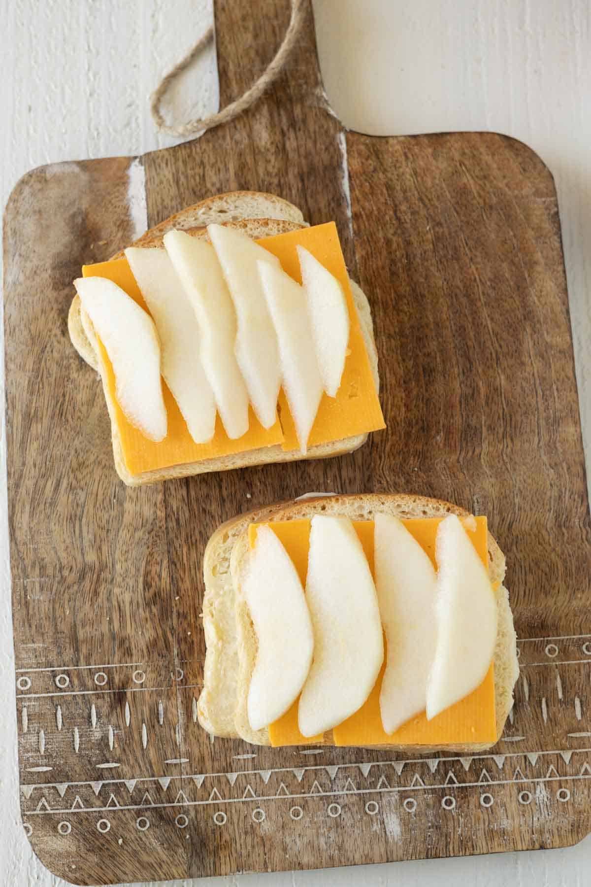 A slice of bread with cheddar cheese and sliced fresh pears.