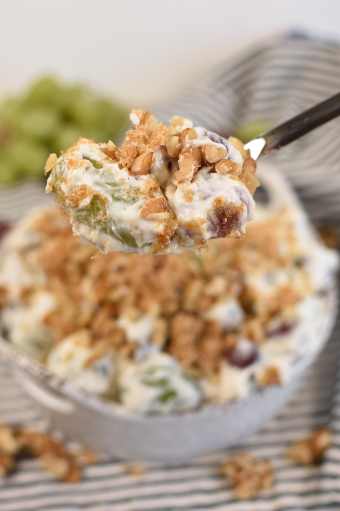 A serving spoon of grape salad with a blurred out image of a bowl of grape salad in the background