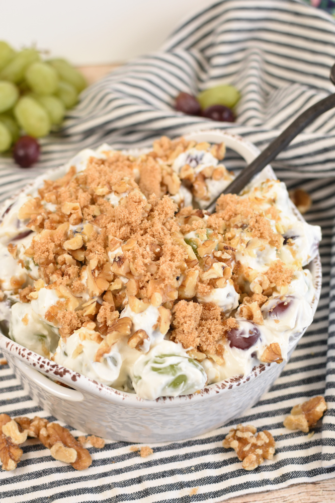 Grape salad with a spoon in it and walnuts on a black and white napking