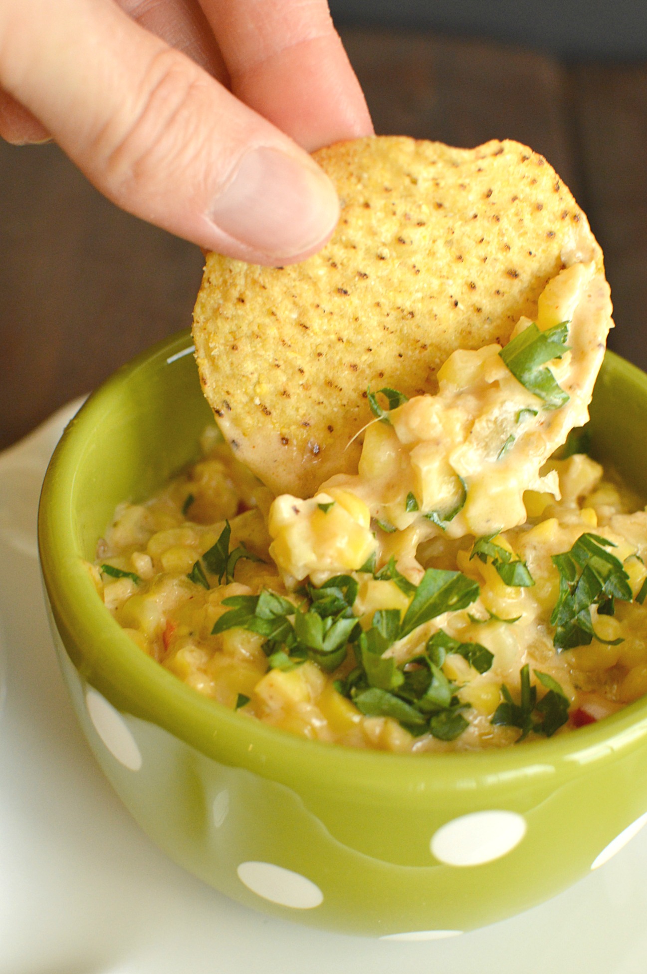 a green bowl with white polka dots with creamy dip made with corn and a tortilla chip dipping into the corn.