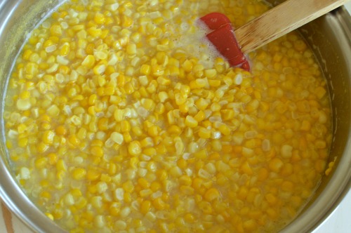 a pan with corn kernels boiling in water with a red spatula