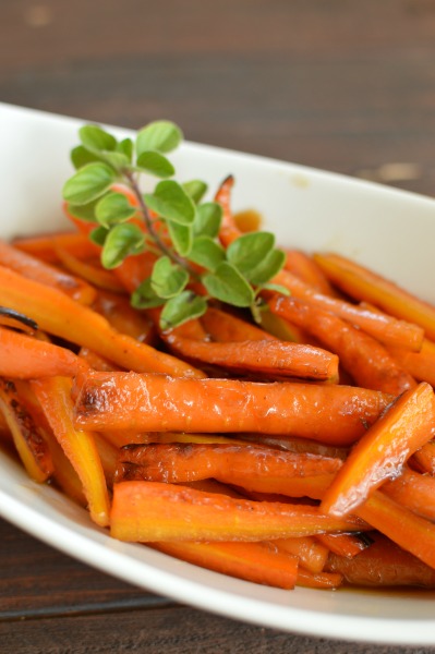 a white dish with roasted carrot sticks and a sprig of thyme