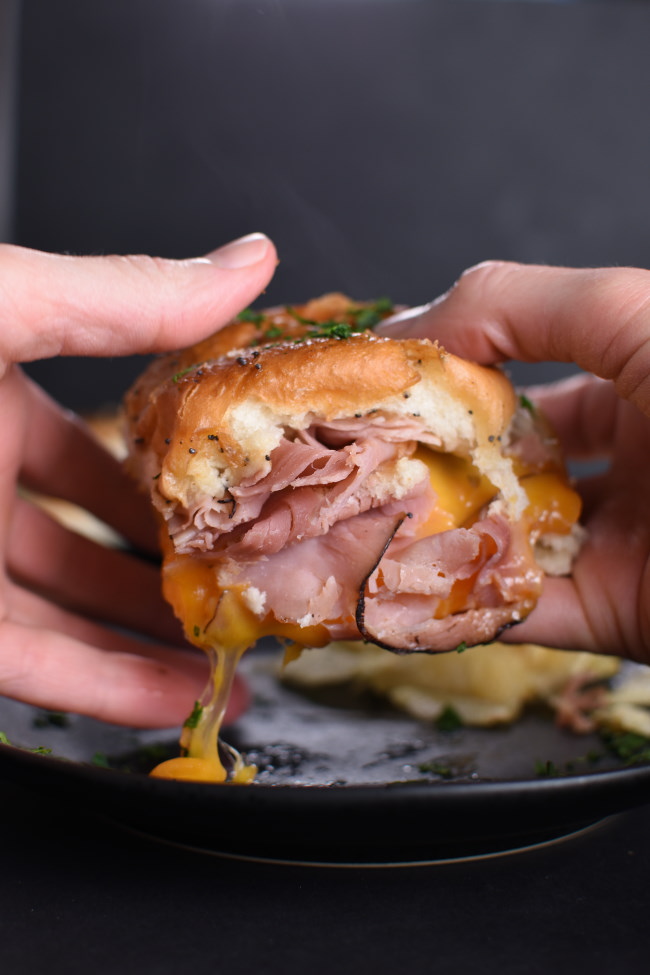 a baked ham and cheddar slider being held by two hands