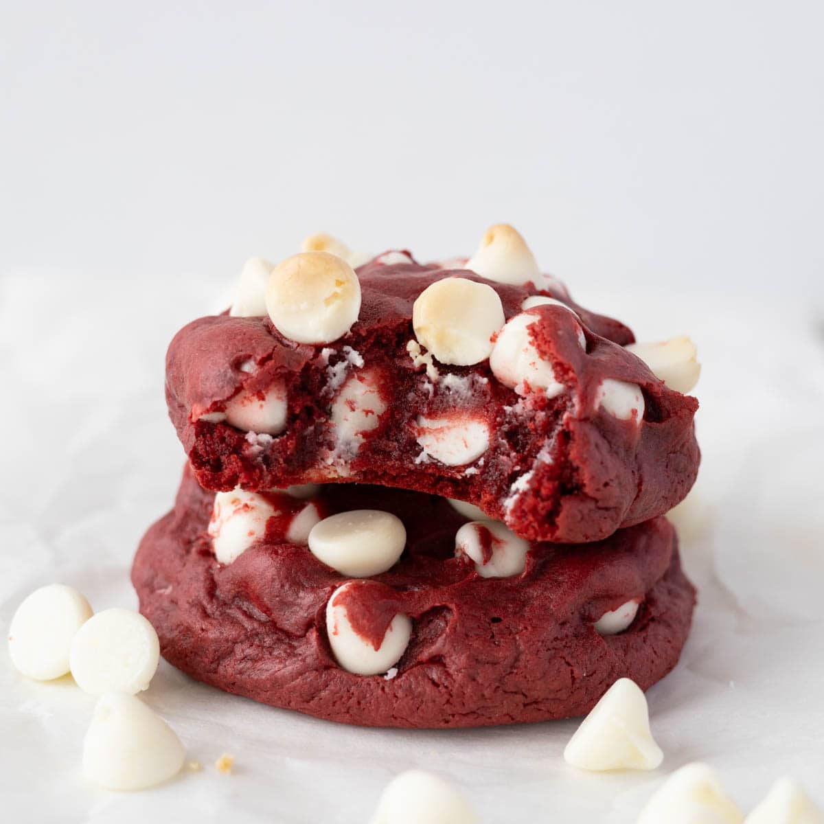 Two red velvet white chocolate chip cookies stacked on top of each other with a bite out of the top cookie.
