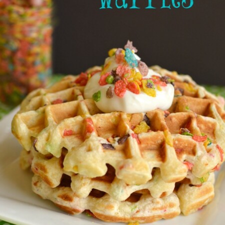 A stack of waffles with fruity pebbles in them, topped with whipped cream and more fruity pebbles cereal