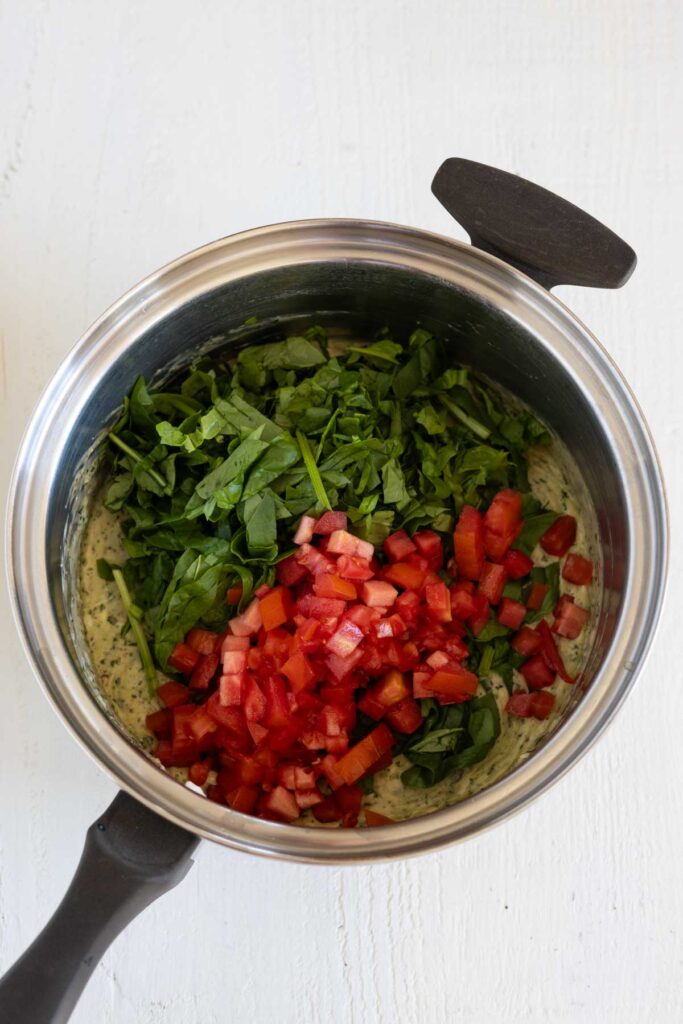 A saucepan with creamy sauce topped with spinach and tomatoes. 