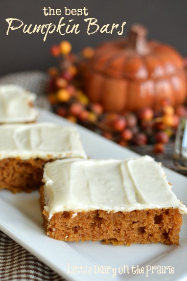 pumpkin bars with cream cheese icing on a white tray with a pumpkin in the background