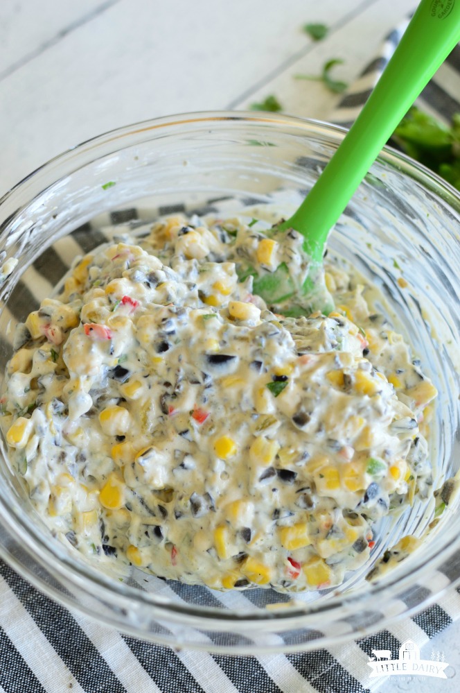 Skinny Poolside Dip- a glass bowl with creamy dip with corn, chopped olives, red peppers, and jalapenos