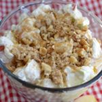 a glass bowl with creamy apple salad topped with brown sugar streusel