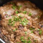 Cube steak in a slow cooker with chopped parsley on top.