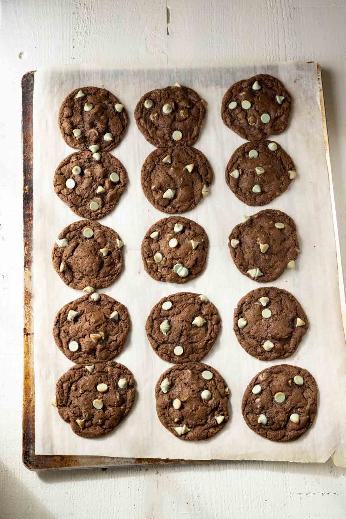 Baked chocolate cookies with green mint chips on a parchment paper lined baking sheet.
