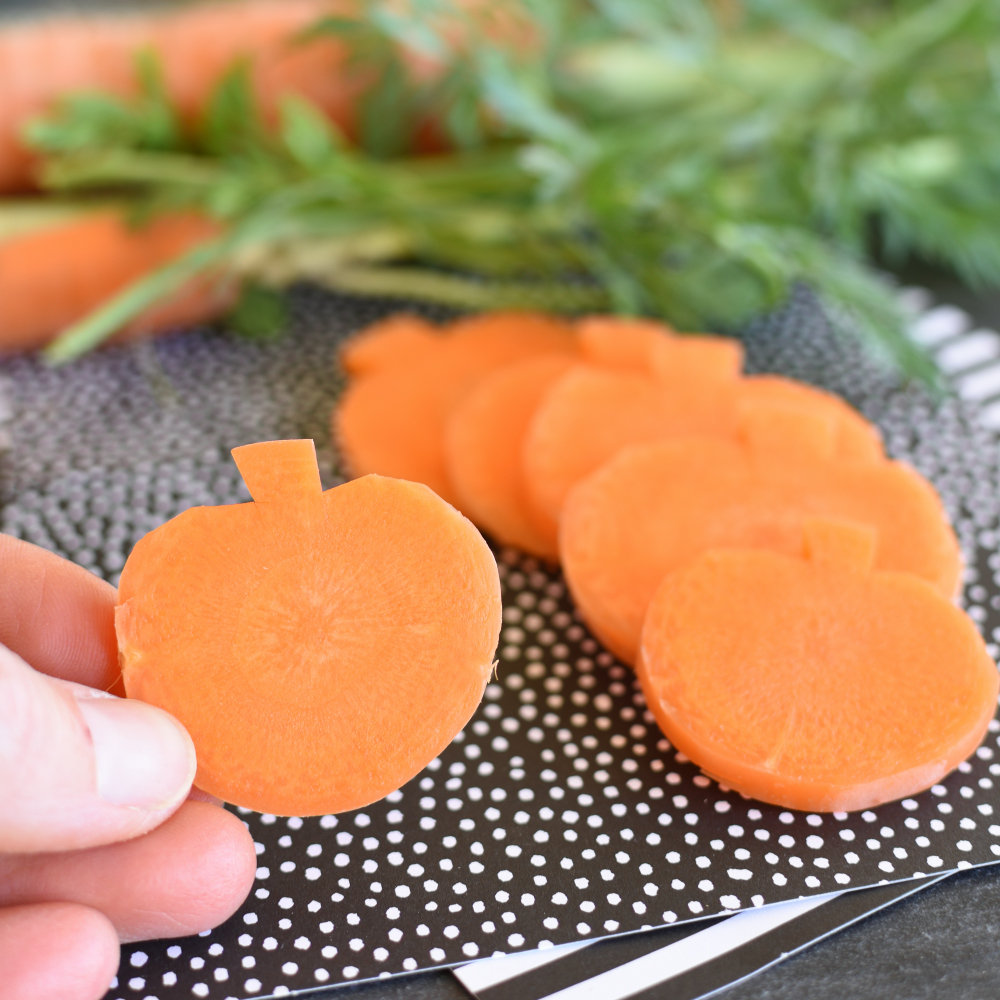 carrots carved to look like pumpkins on a black piece of paper make a healthy Halloween snack