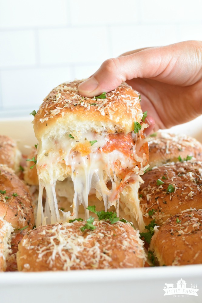 A hand holding a pepperoni pizza slider with cheese stringing.
