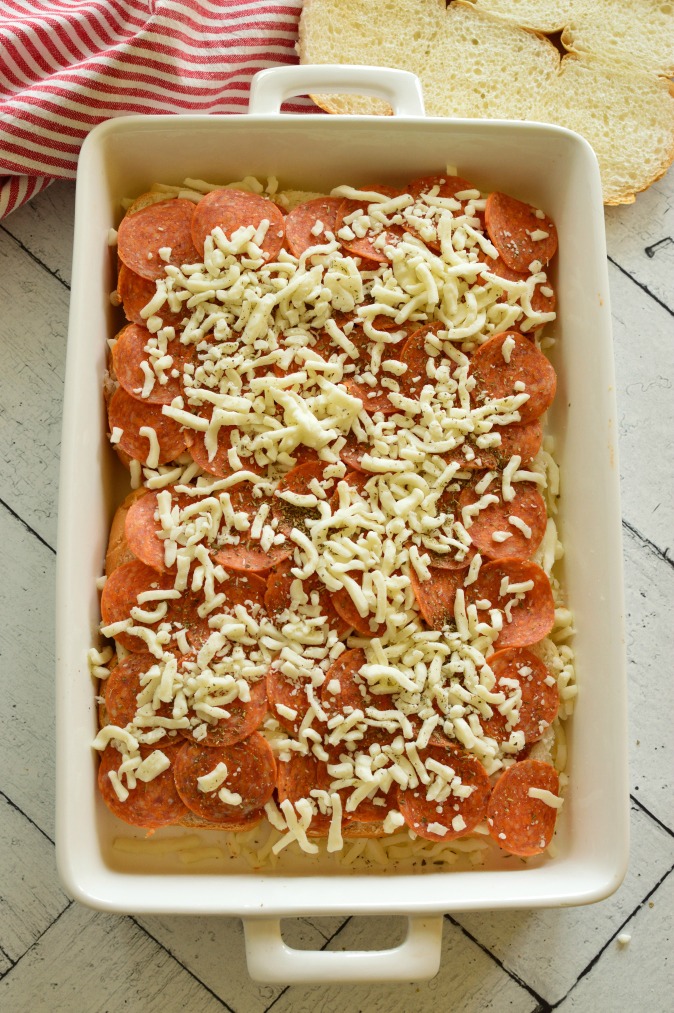 Sliders in a white baking dish with grated cheese and pepperoni 