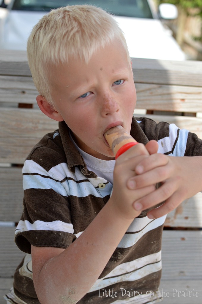 a boy eating a popsicle on a wooden bench