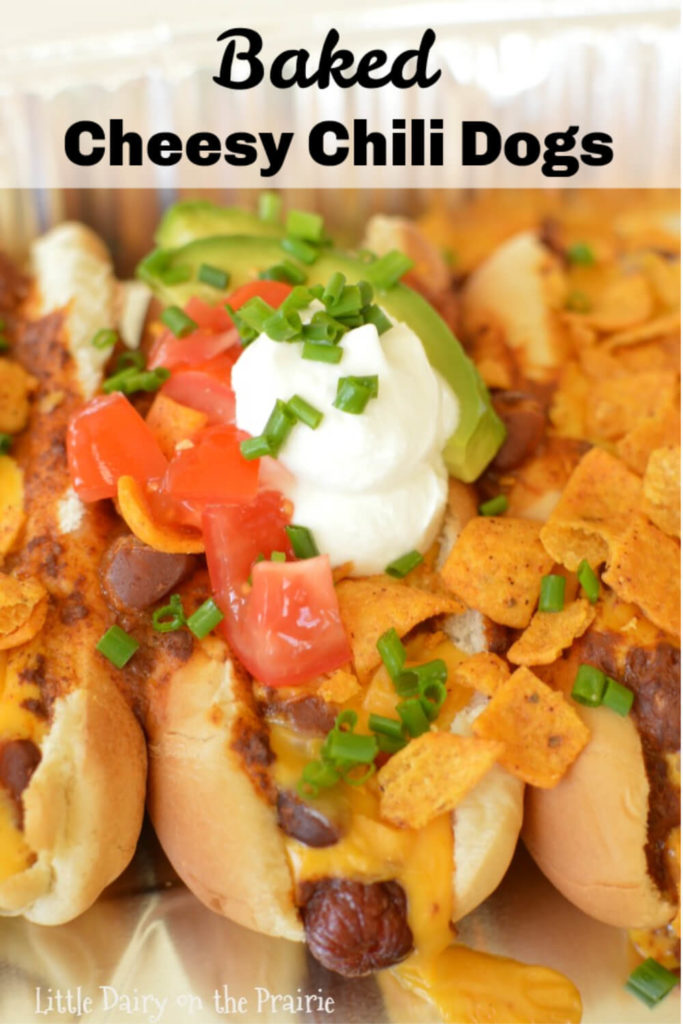 a pan with hotdogs covered with chili, cheese, diced tomatoes, onions, sour cream, and chips