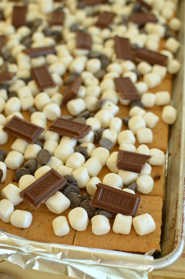 a baking sheet with marshmallow and chocolate chips on graham crackers