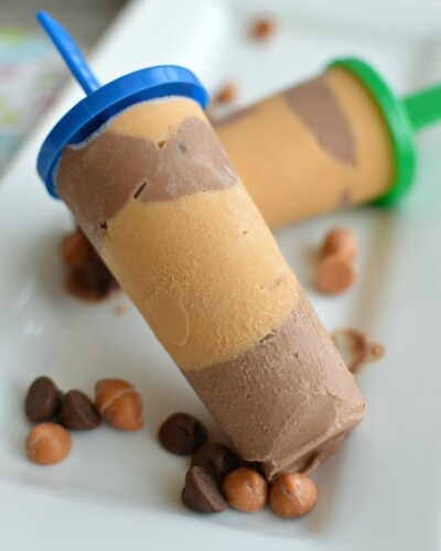 a popsicle with peanut butter layers and chocolate layers on a white plate sprinkled with chocolate chips
