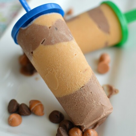 a popsicle with peanut butter layers and chocolate layers on a white plate sprinkled with chocolate chips
