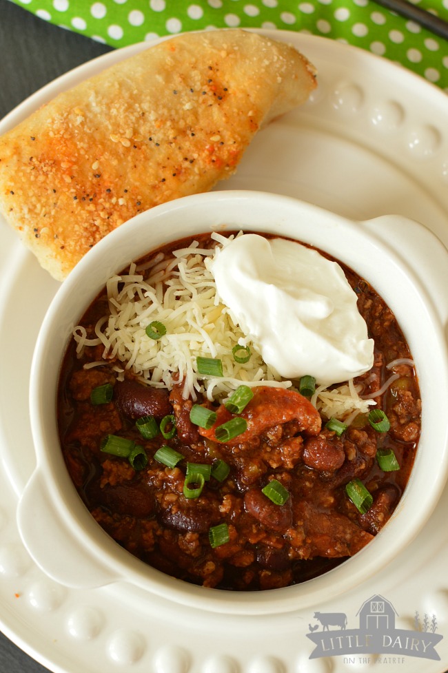 a bowl of chili topped with green onions, grated parmesan cheese, and sour cream