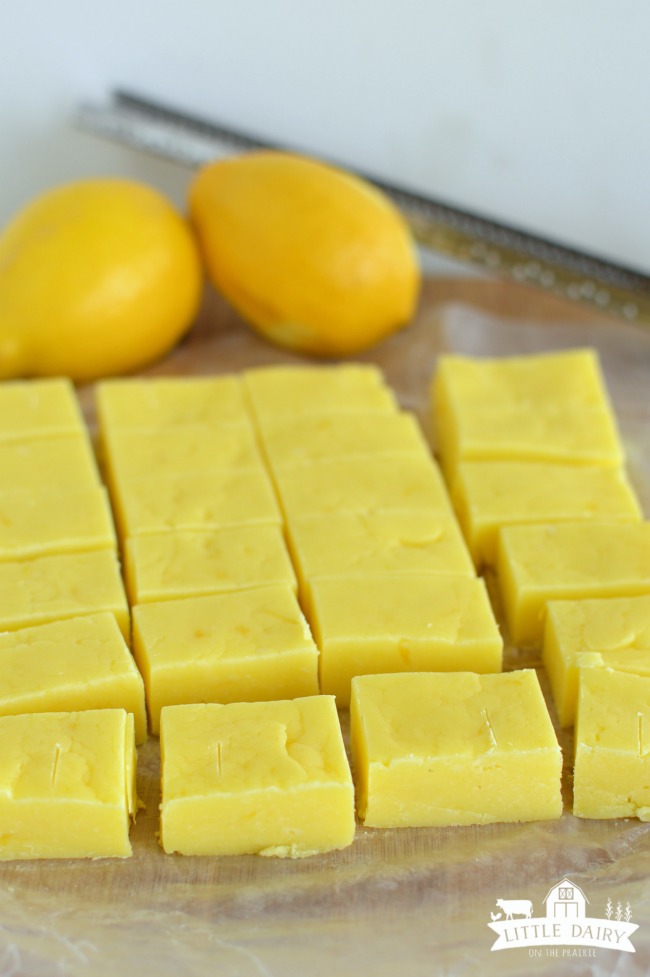 Yellow lemon fudge cut into pieces with fresh lemons in the background.