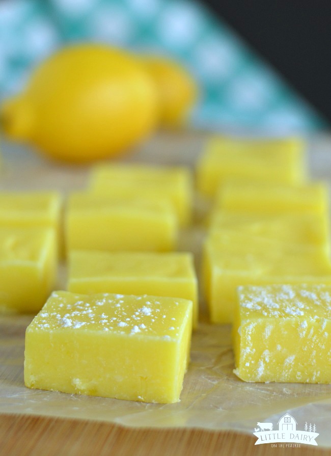 Squares of lemon fudge dusted with powdered sugar on a piece of paper.