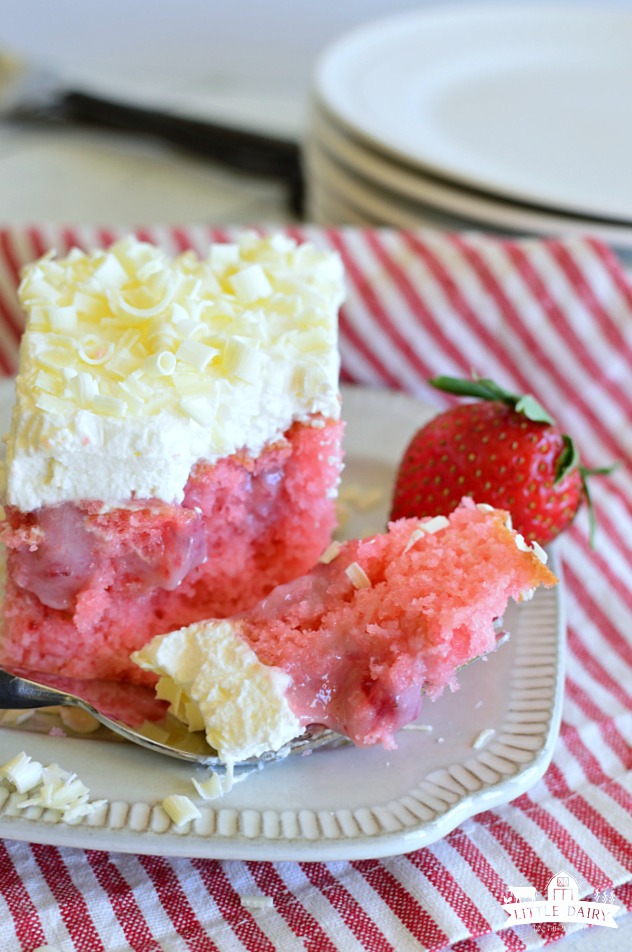 a piece of strawberry cake with a bit on a fork, a fresh strawberry in the background