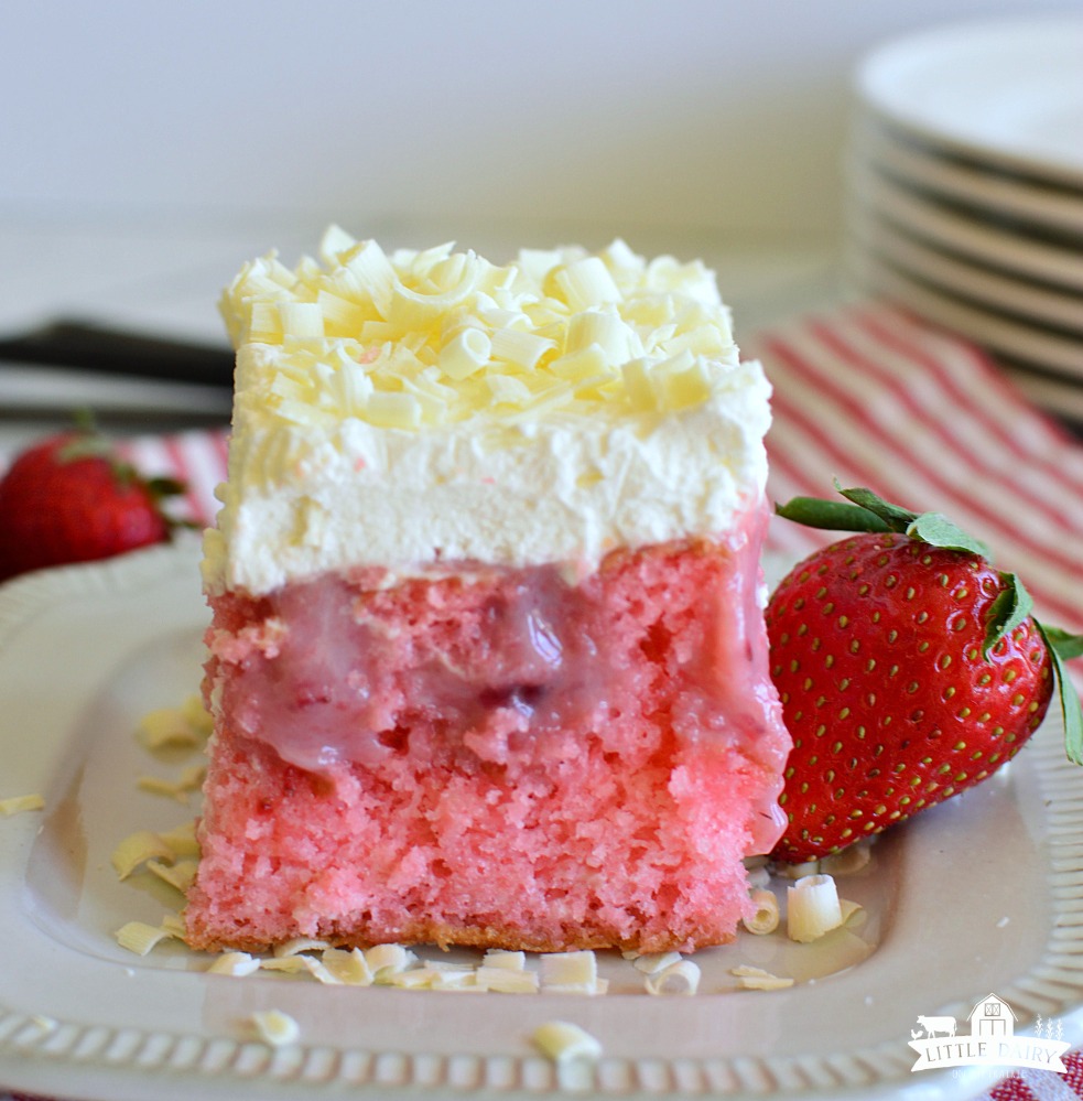 a square of pink strawberry cake topped with whipped cream and white chocolate curls