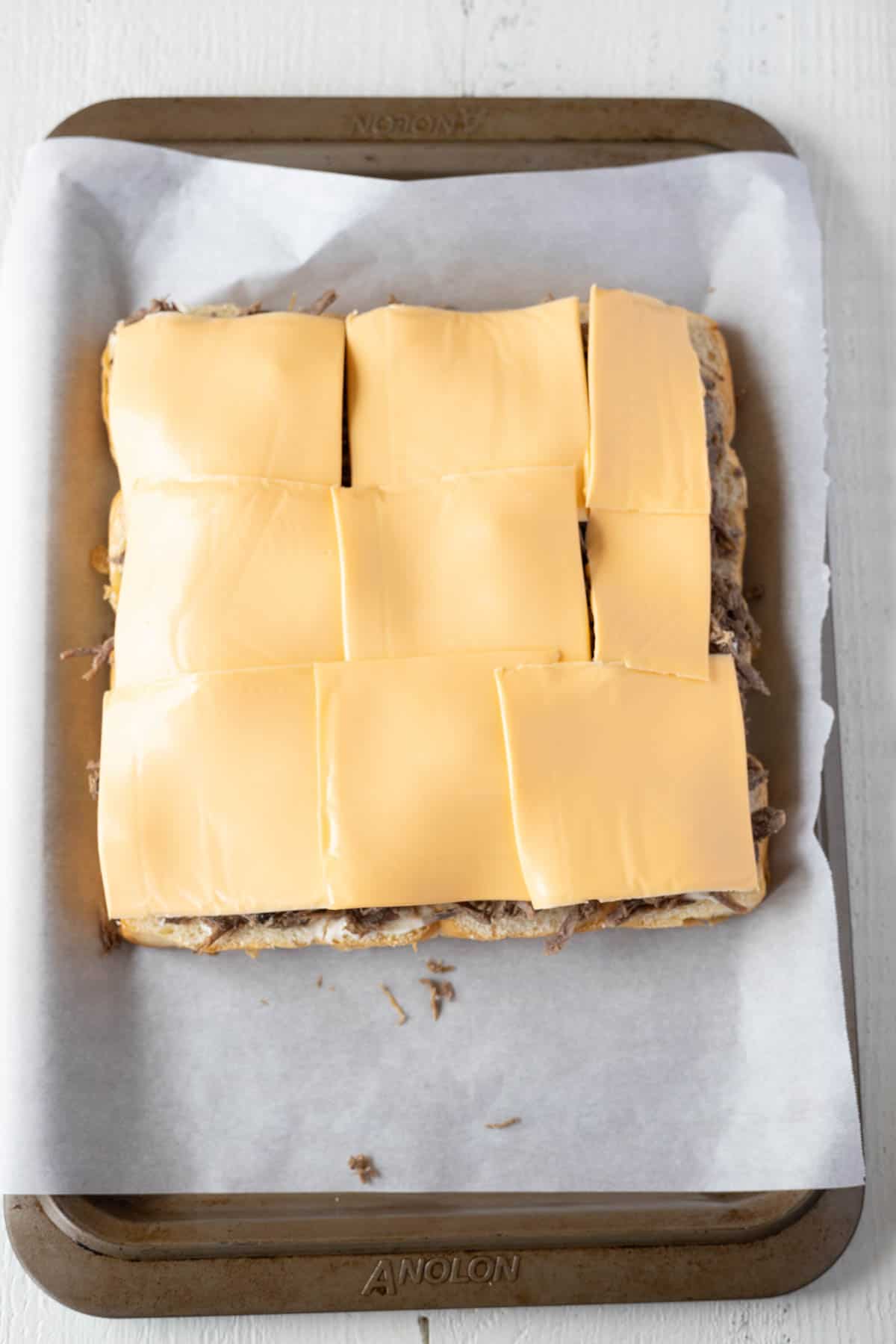 Roast beef sliders with a layer of slices of American cheddar cheese layered over the roast beef.