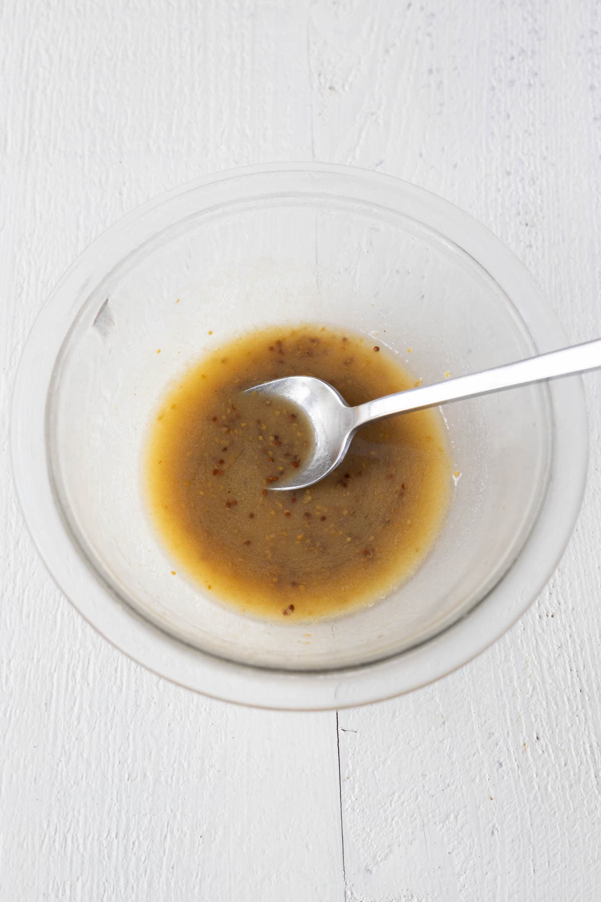Melted butter and mustard sauce in a glass mixing bowl with a spoon.