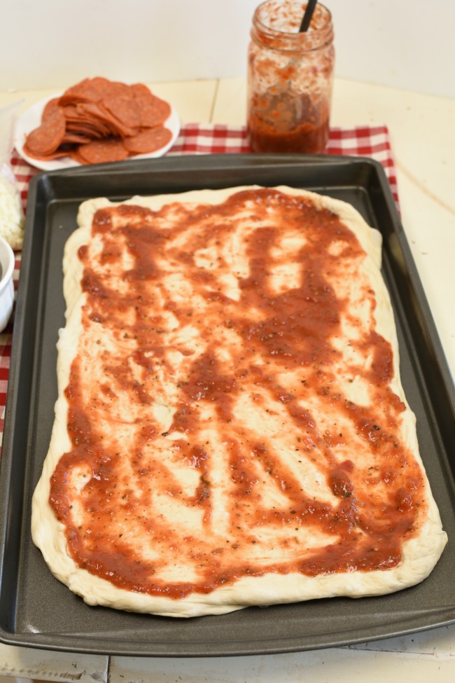 A cookie sheet with dough and marinara sauce spread over it.