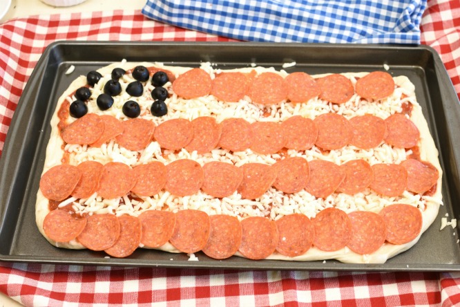 Pizza with olives for stars and pepperoni for stripes in a sheet pan.