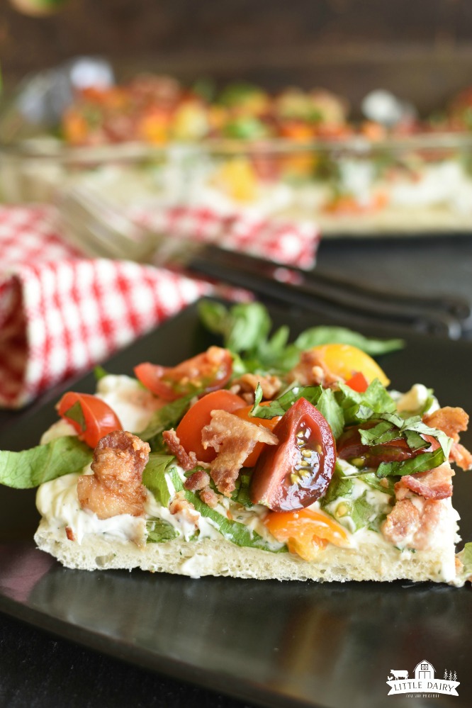 a square of cold pizza with bacon, lettuce, and tomatoes on top