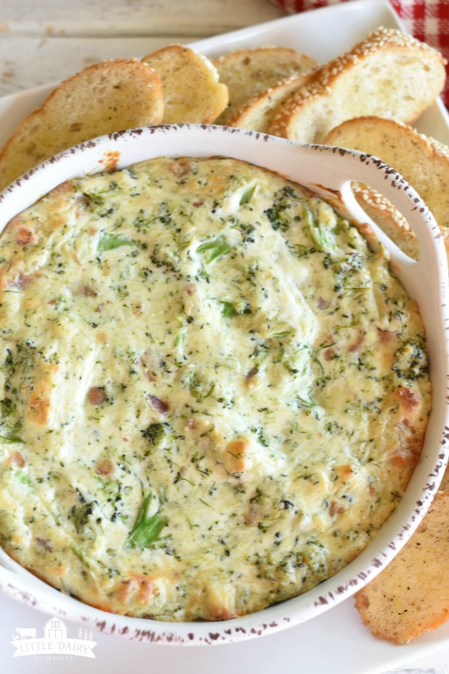 a baking dish with cream cheese dip with pieces of broccoli and bacon