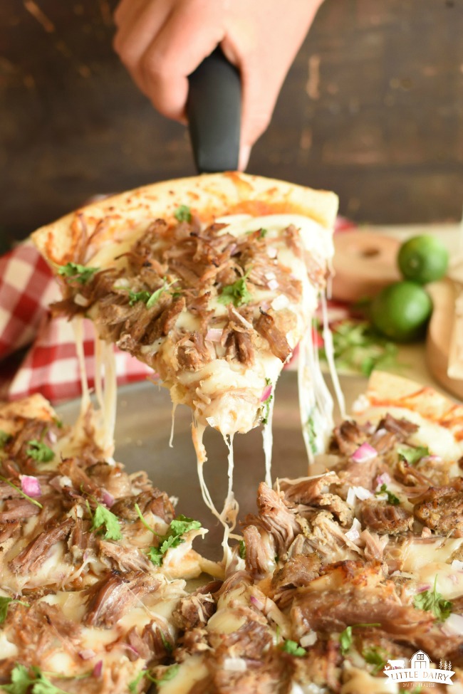 a slice of pizza topped with carnitas meat, mozarella cheese, chopped cilantro, with a wedge of lime