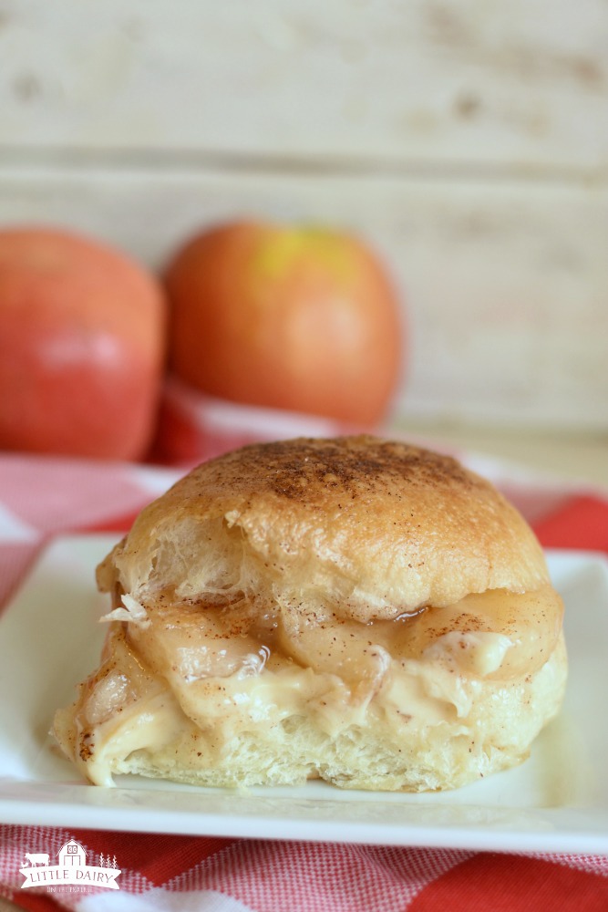 a white dinner roll with apple pie filling and cheesecake in the middle of it. The top of the roll is brushed with butter and sprinkled with cinnamon sugar.