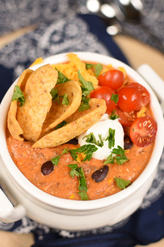 a white bowl with taco soup topped with corn chips, sliced cherry tomatoes, cilantro, and cilantro