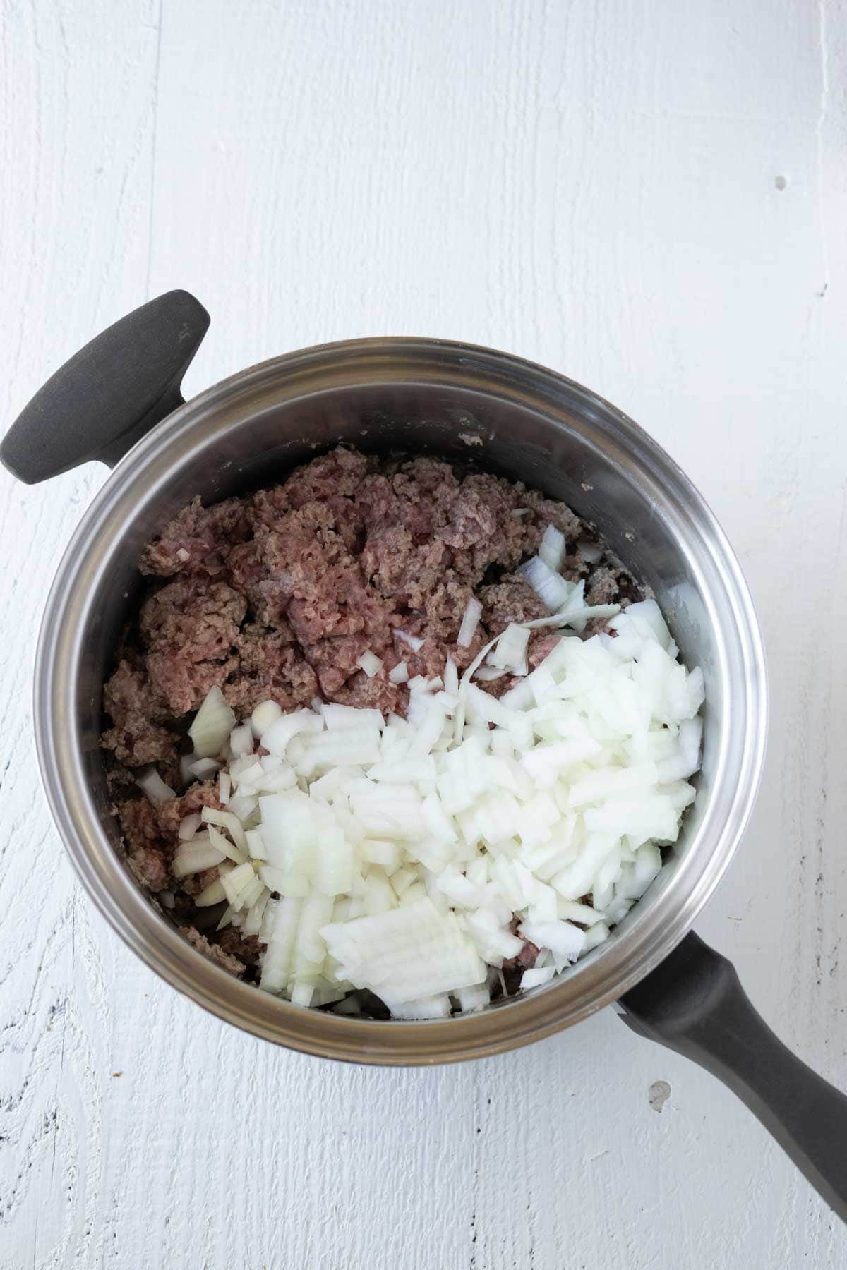 A saucepan with browned ground beef and diced onions.