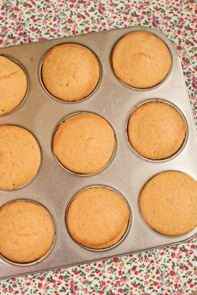 a muffin tin with baked cornbread muffins on a floral napkin