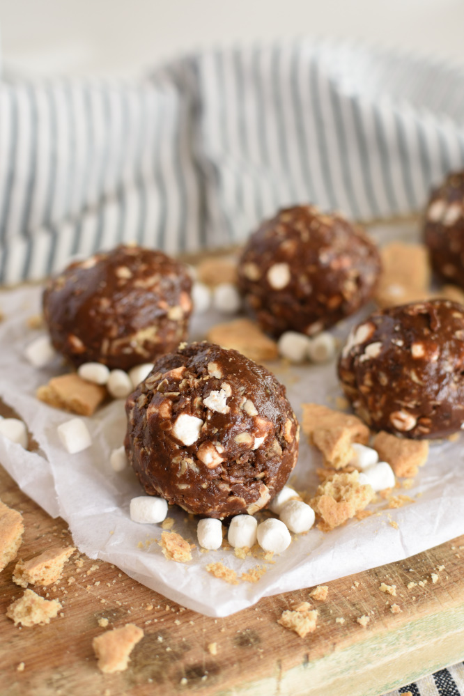 S’mores Energy Bites have all the chocolatey goodness you can handle wrapped up in this little treat! Add ins like marshmallows and graham cracker chunks pack in all the campfire favorite flavors without all the guilt! You just can’t beat that! Okay, can we be honest with each other for a minute here? When I add a recipe to my blog and claim it’s “skinny” or “healthy” I’m kind of just guessing because I don’t count calories, fat grams, carbs, or whatever else people count when they are determining if something is healthy! So how do I decide if a recipe is healthy? Well, here’s the unscientific method! If I substitute Greek yogurt in for mayo it’s automatically healthy! If it has fruits and veggies without lots of creamy dressing it’s just HAS to be healthy! Whole wheat instead of white flour means it’s better for you right? And if it doesn’t have refined or artificial sugar it’s a thinny skinny recipe for sure! There you have it! That’s how I roll! Who has time for math and calculating calories anyway? I’d rather spend that time jogging in order to earn a treat! S’mores Energy Bites are made with honey instead of sugar so that means they are healthy in my book! Wahoo! Okay, so they do have a few sugary add ins but you know...there are only a few of them! I’m not sure anyone understands how badly I get chocolate cravings right after lunch and again right after dinner! My friends tell me they get the most intense chocolate cravings about once a month...what? Only once a month? I get them twice EVERY. SINGLE. Day! No joke! I’ve learned it’s best for me to give in to it. Just embrace it and move on. If I can have a little piece of chocolate as soon as my meal is gone I’m completely okay and can move on with my life. If I don’t get my chocolate...I pretty much can’t think of anything else except chocolate. I scrounge through my cupboards and pantry until I get my fix. Yes! I’m addicted! Who cares! S’mores Energy Bites are one of my favorite healthy (according to my standards) little treats out there! They taste incredible! There is no chalky texture or aftertaste with these either. (I’m not into protein powders, diet shakes, etc.) Whip up a batch of S’mores Energy Bites and keep them in the fridge for when that crazy chocolate craving attacks you! No what else is awesome about them...just one energy bite knocks the cravings! That’s right...one little ball! My kids love them in their lunches. I like to stick a couple in my purse because I already know I’m going to need chocolate! They even make a pretty delicious on the go breakfast option! It only takes about 5 minutes to whip them together. Well, that’s not true. You have to refrigerate them before you roll them in balls. So, go take a shower or something while they are in the fridge, come back and they’ll be ready for ya! S’mores Energy Bites have enough cocoa in them to give them that intense chocolate flavor, natural peanut butter and honey give them the best texture, and then there’s the graham crackers and marshmallows! I’ve never tasted more scrumptious “healthy” campfire treat! S’mores Energy Bites pack all the campfire favorite flavors right in there! If you are a calorie counter, or whatever else kind of counter please don’t tell me these aren’t healthy! In my mind they are and I want to keep believing it! Plus, they can’t be as bad as eating a candy bar! There you go! Grab a S’mores Energy Bite for breakfast, dessert, or a snack. No guilt with this one! 