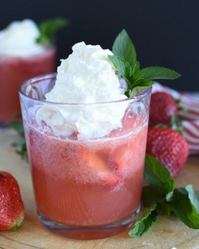 A fizzy strawberry drink in a glass with whipped cream on top of it.