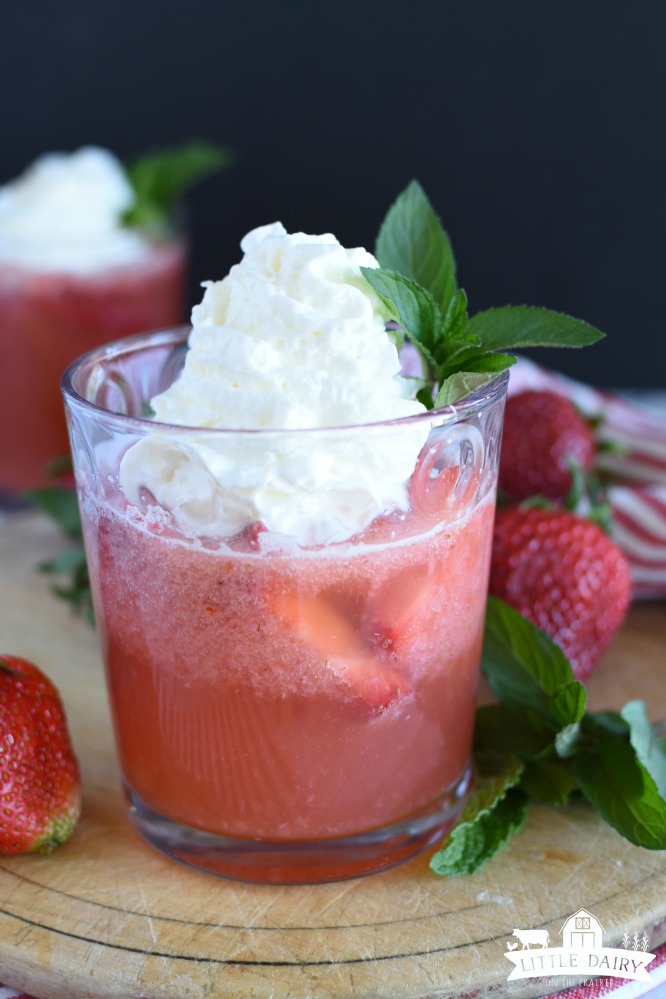 A fizzy strawberry drink in a glass with whipped cream on top of it.