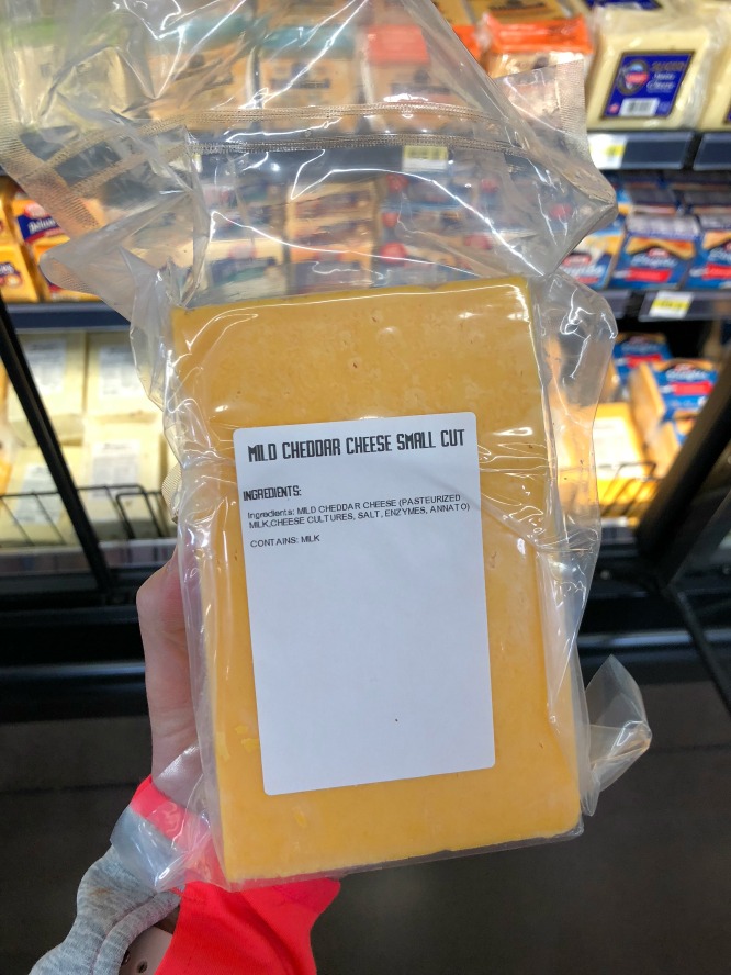 A block of yellow cheddar cheese in a plastic wrap