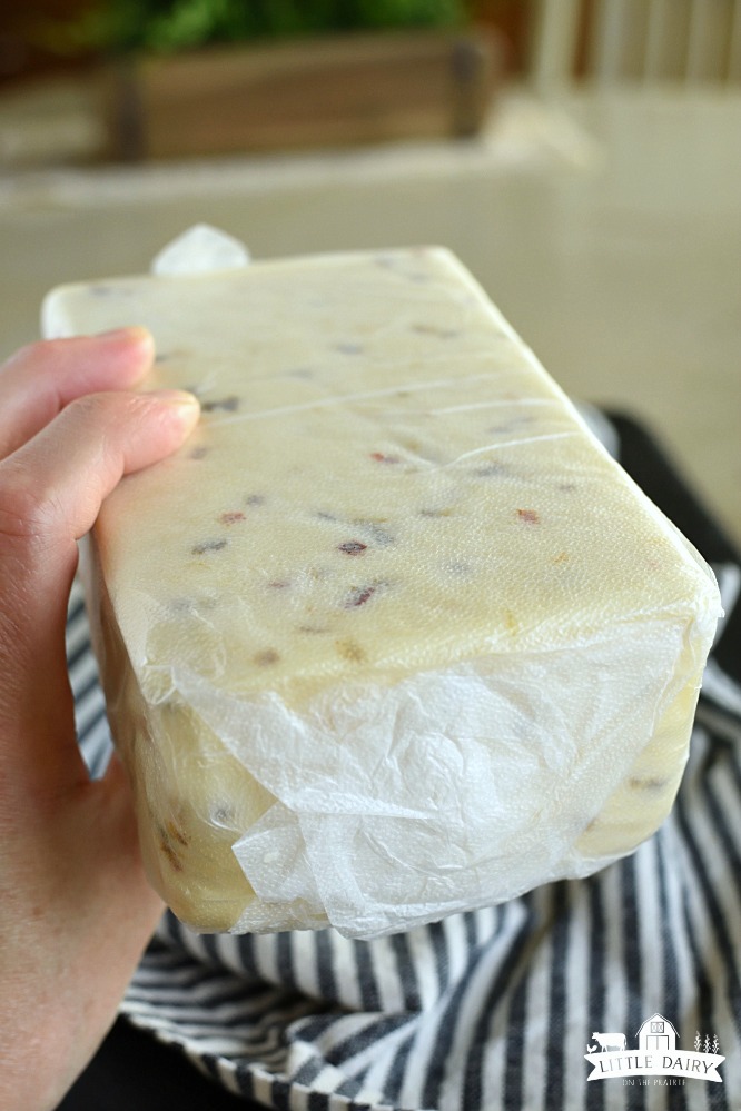 Brick of Pepper Jack cheese wrapped in press and seal wrap, held in a hand 