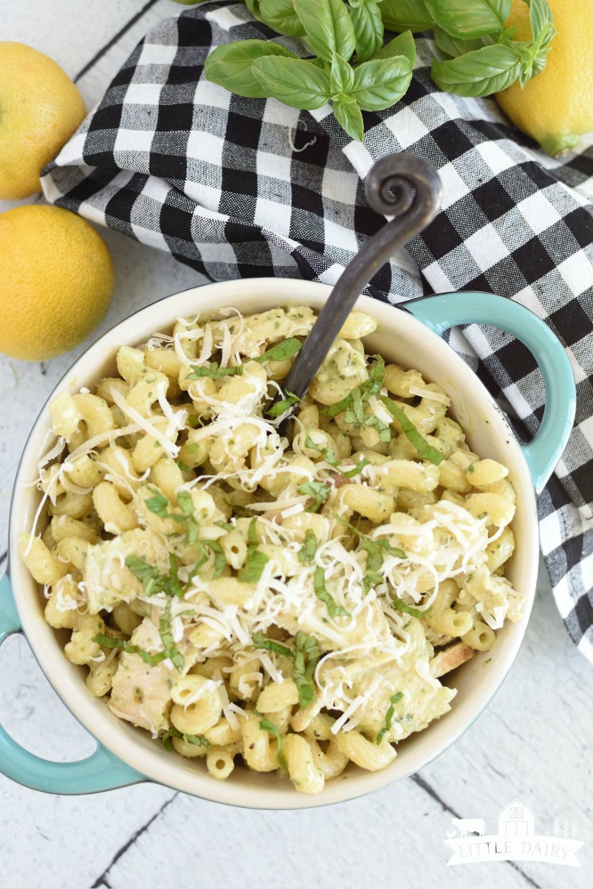 overhead view of pesto pasta in a turquoise bowl, with lemons in the background on a black and white checkered napkin